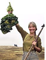 Me, holding up kale, with my farm behind me