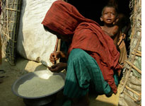 A boy cries and leans on his mother while she separates rice in front of their hut in Teknaf. Click image to expand.