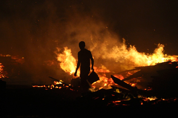 A man holds a bucket as he tries to extinguish a late night fire at the Okobaba sawmill near the Lagos Lagoon January 8, 2013.