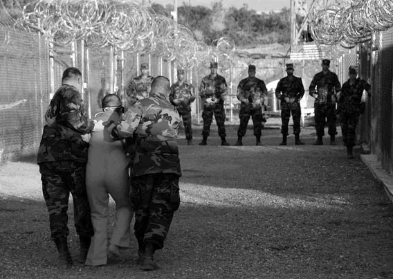 U.S. Military Police guard Taliban and al Qaeda detainees in orange jumpsuits January 11, 2002 in a holding area at Camp X-Ray at Naval Base Guantanamo Bay, Cuba during in-processing to the temporary detention facility. 