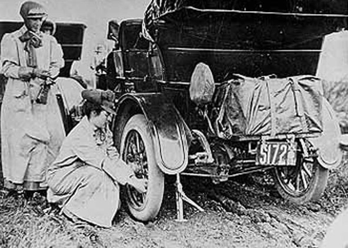 Alice Huyler Ramsey (1887-1983) in 1909. Asphalt roads were a rarity and repairs frequent during the pioneer cross-country drive of Alice Huyler Ramsey in 1909. Shown here changing a tire on her green Maxwell