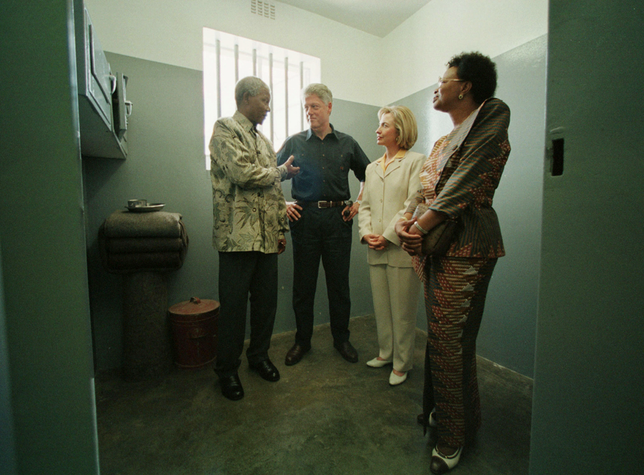 South African President Nelson Mandela talks to Bill and Hillary Clinton March 27 from inside his former prison cell on Robben Island where he spent 18 years. Clinton said he was glad Mandela survived the experience without &quot;having his heart turned into stone.&quot; At right is Mandela's partner Graca Machel.