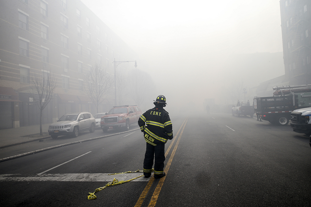 A firefighter stands on smoke-filled East 116th Street.