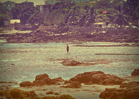 A man walks along the beach during low tide in Conakry, Guinea