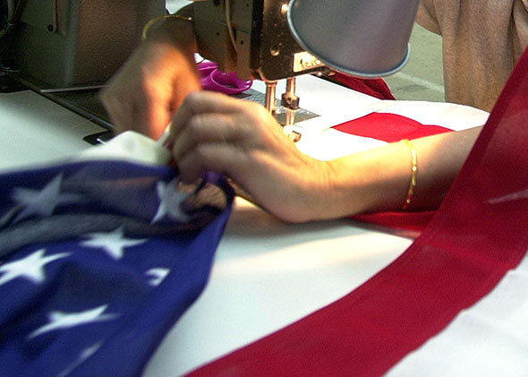 A woman adjusts her sewing machine as she sews an American flag 