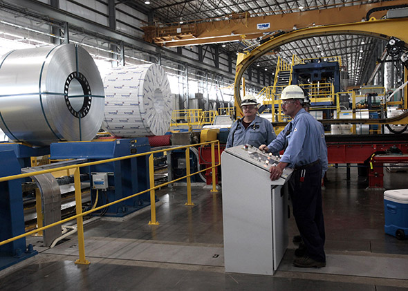 Steel workers stand by the operating station for shrinking wrapping steel coils in a steel mill.