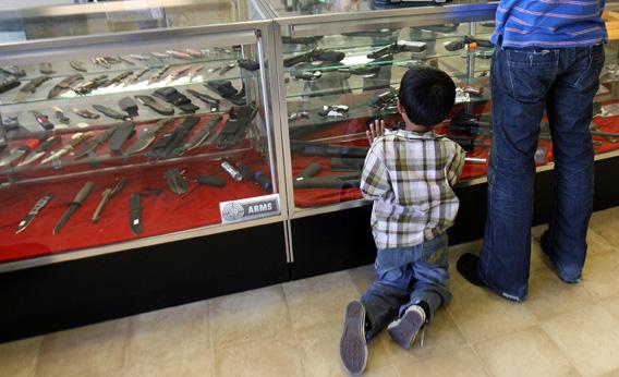 A boy looks at guns in a case.