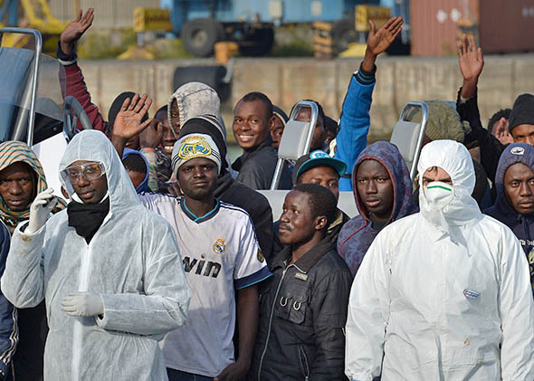 Rescued migrants wave as they disembark off the Italian Guardia di Finanza vessel Denaro upon arrival to the Sicilian harbour of Catania on April 23, 2015. 