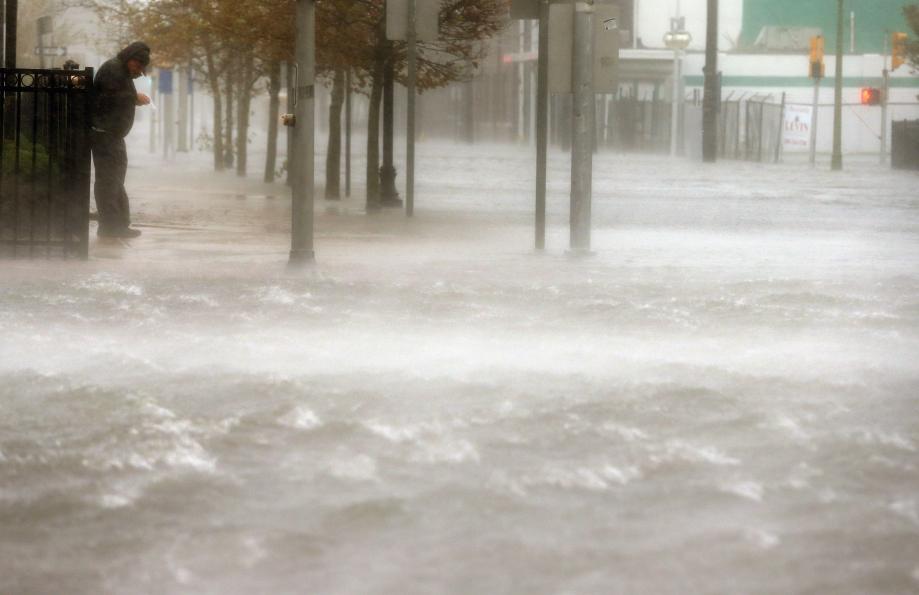 A man stands on a dry patch of sidewalk on a flooded street as Hurricane Sandy moves up the coast on Monday in Atlantic City, New Jersey.