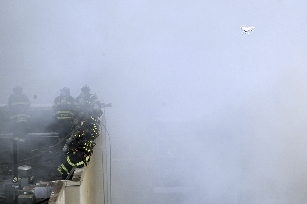 Firefighters respond to the building collapse as a drone flies overheard.