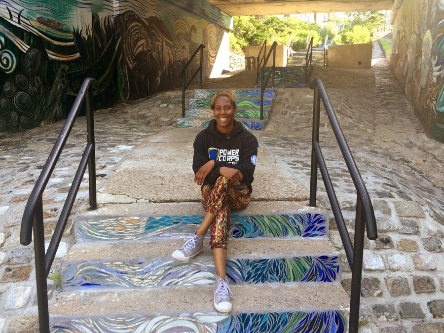 Hill poses on colorful steps painted by a PowerCorps team. After 8 hours at this job, she&rsquo;ll head to her next job sorting recyclables, before heading home to do it all again the next day. 