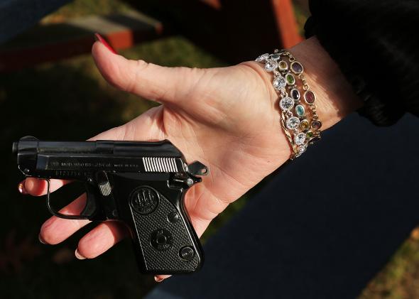 158638982-woman-holds-a-beretta-pistol-at-a-gun-buyback-event-at